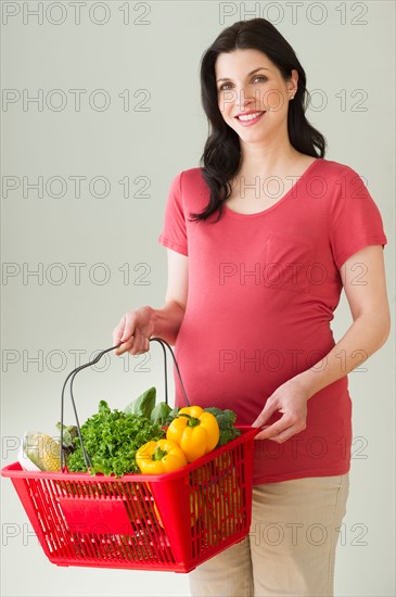 Studio portrait of woman with shopping basket full of groceries.