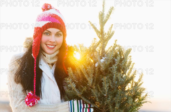 Portrait of young woman carrying Christms tree.