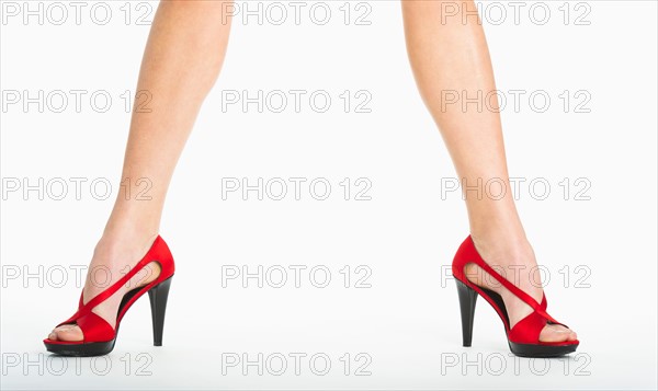 Low section of woman wearing red shoes on white background.