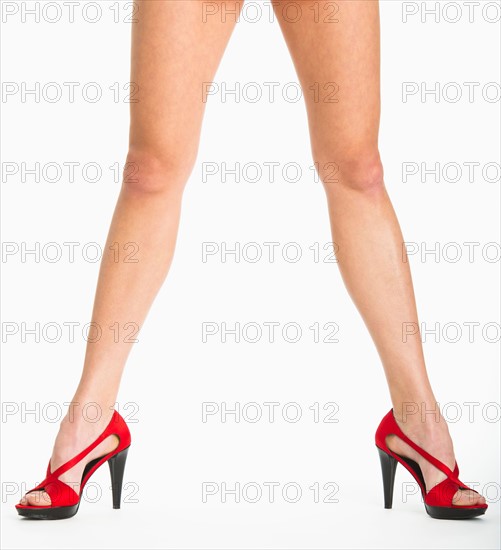 Low section of woman wearing red shoes on white background.