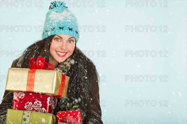 Studio portrait of woman in winter clothing carrying presents.
