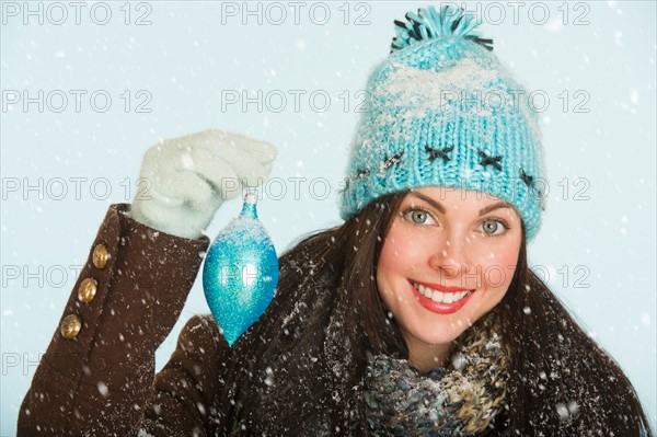 Studio portrait of woman in winter clothing holding Christmas ornament.