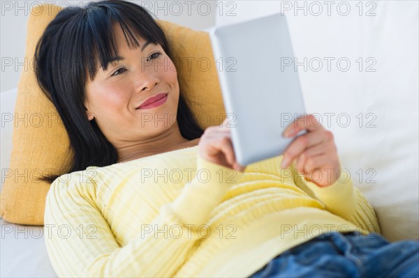 Smiling woman lying on sofa and using digital tablet.