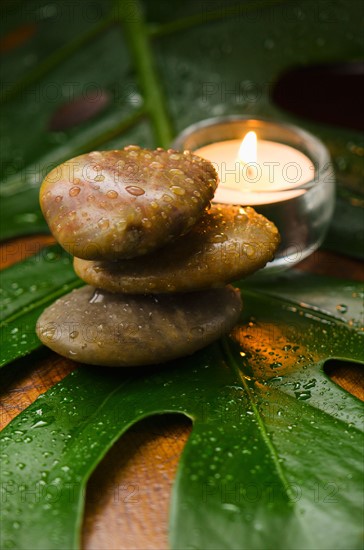 Spa stones and candle on tropical leaf, studio shot.