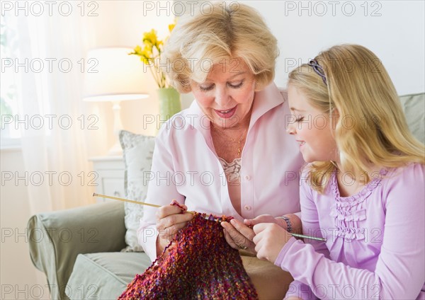 Grandmother with granddaughter (8-9) knitting at sofa.