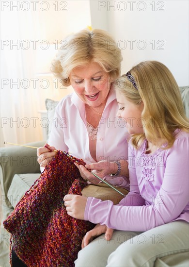 Grandmother with granddaughter (8-9) knitting at sofa.