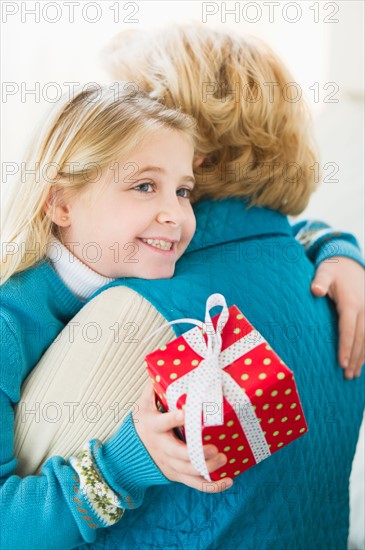 Granddaughter (8-9) hugging grandmother and holding gift.