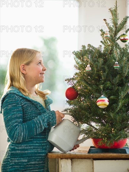 Girl (8-9) watering Christmas tree.