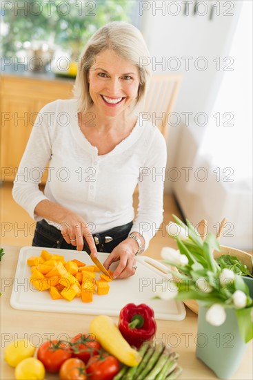 Portrait of senior woman cutting vegetables in kitchen.