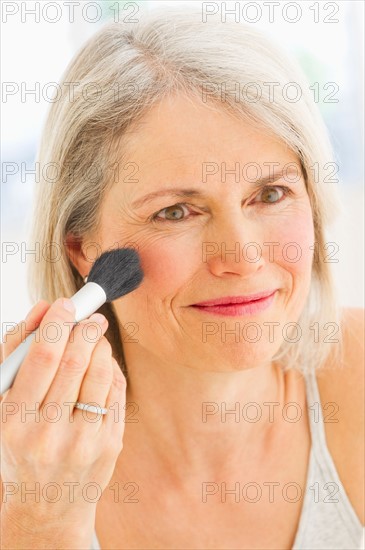 Portrait of senior woman applying blush.