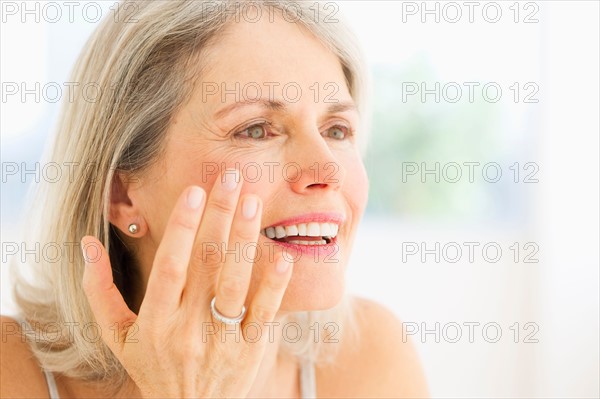 Portrait of senior woman applying moisturizer.