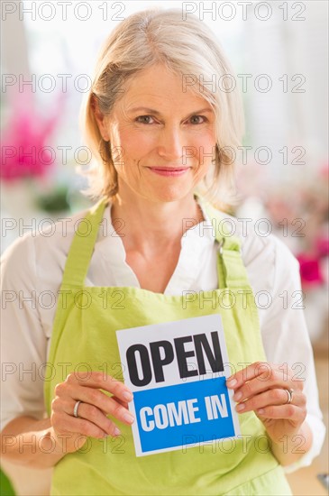 Portrait of senior female florist showing open sign and smiling.