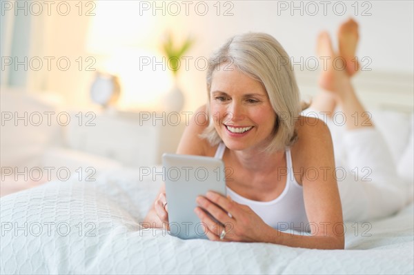 Senior woman lying on bed and using digital tablet.