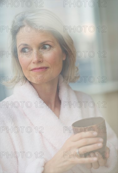 Senior woman looking through window in morning.