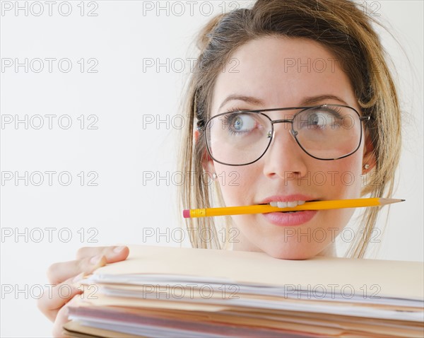 Portrait of young woman wearing glasses and holding pencil in mouth, studio shot.