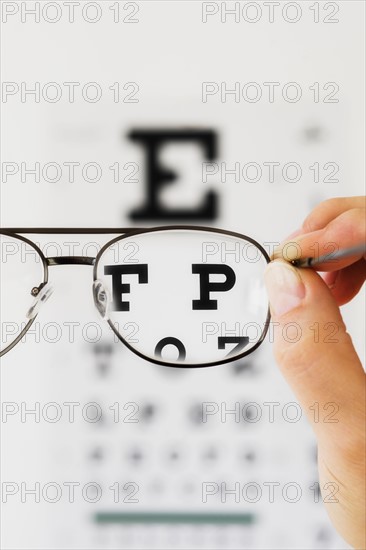 Close up of hand holding glasses above eye chart, studio shot.