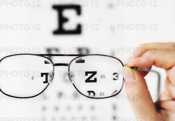 Close up of hand holding glasses above eye chart, studio shot.