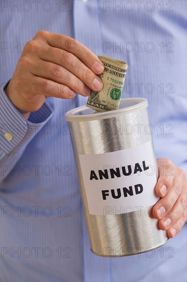 Man putting dollars into annual fund can.