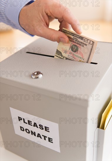 Man's hand putting dollars into donation box.