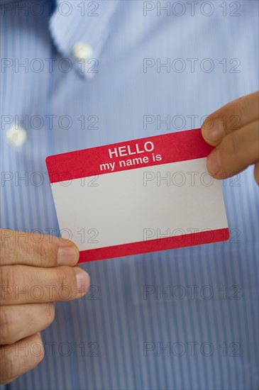 Close up of businessman's hands holding blank name tag, studio shot.