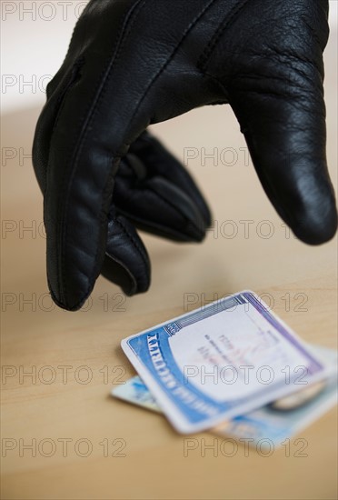 Close up of thief's hand in black glove stealing driver's license, studio shot.