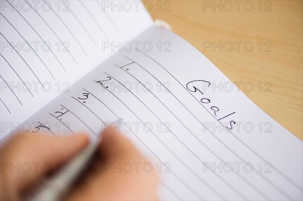 Close up of man's hand writing New Years resolution in notebook, studio shot.