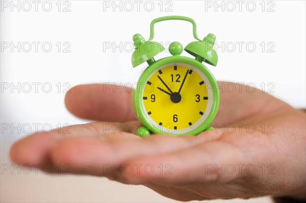 Close up of man's hand holding alarm clock, studio shot.