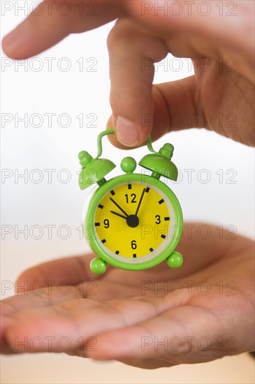 Close up of man's hand holding alarm clock, studio shot.