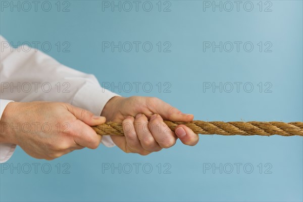 Close up of man's hands pulling rope, studio shot.