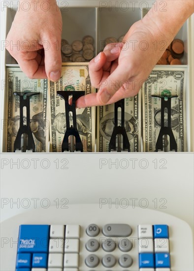 Close up of man's hand putting banknotes into cash register, studio shot.