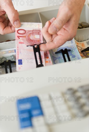 Close up of man's hand putting banknotes into cash register, studio shot.