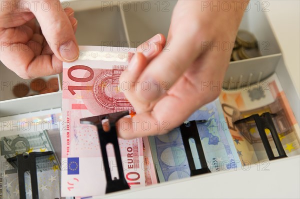 Close up of man's hand putting banknotes into cash register, studio shot.