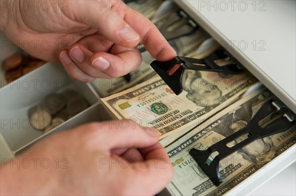 Close up of man's hand putting banknotes into cash register, studio shot.