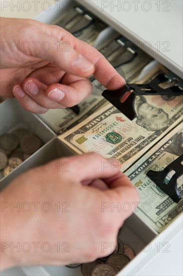 Close up of man's hand putting banknotes into cash register, studio shot.
