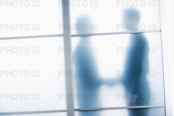 Silhouettes of two businessmen behind glass door.