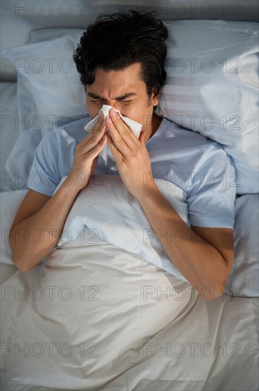 Man lying in bed and blowing nose.