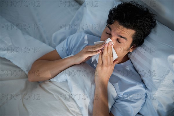 Man lying in bed and blowing nose.