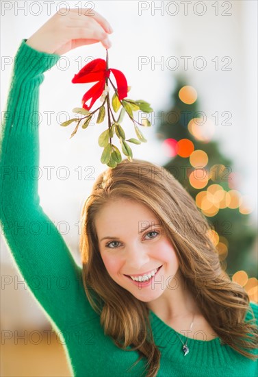 Portrait of young woman holding mistletoe stem over head. Photo : Daniel Grill