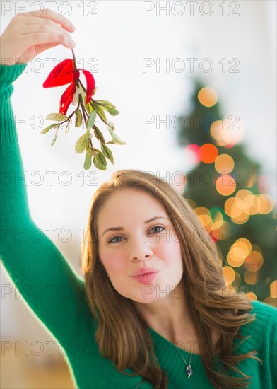 Portrait of young woman holding mistletoe stem over head. Photo : Daniel Grill