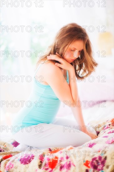 Young woman sitting on bed. Photo : Daniel Grill
