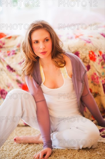 Young woman sitting on floor in bedroom. Photo : Daniel Grill