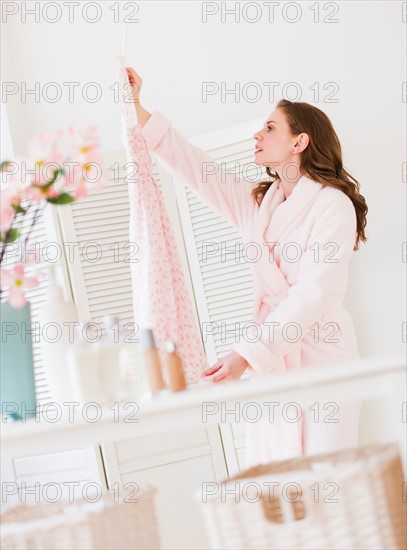 Young woman holding dress in bedroom. Photo : Daniel Grill