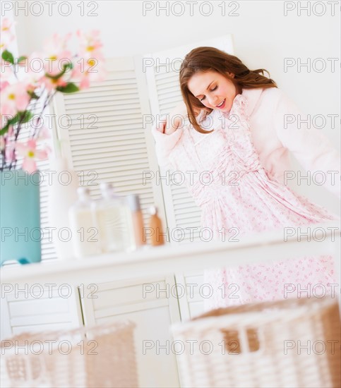 Young woman holding dress in bedroom. Photo : Daniel Grill
