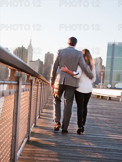 USA, New York, Long Island City, Rear view of young couple walking on boardwalk, Manhattan skyline in background. Photo : Daniel Grill