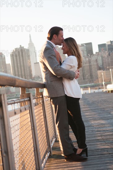 USA, New York, Long Island City, Young couple kissing on boardwalk, Manhattan skyline in background. Photo : Daniel Grill