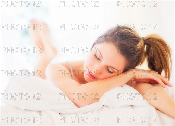 Portrait of young woman lying on bed in bedroom. Photo : Daniel Grill