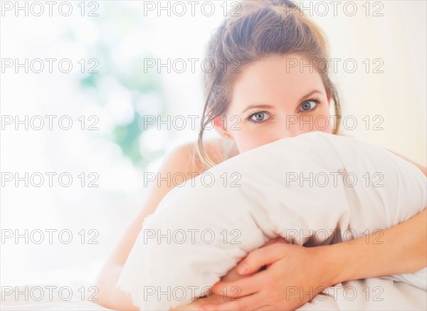 Portrait of young woman embracing pillow in bedroom. Photo : Daniel Grill