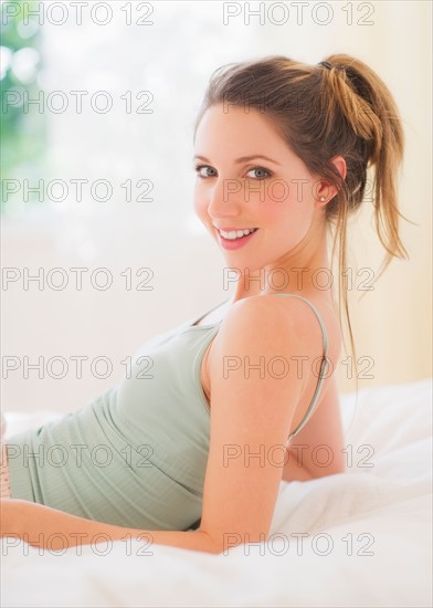 Portrait of young woman lying on bed in bedroom. Photo : Daniel Grill