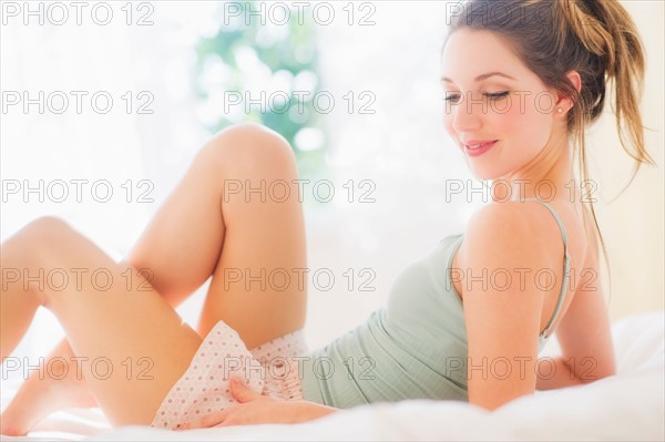 Portrait of young woman lying on bed in bedroom. Photo : Daniel Grill