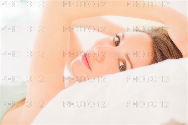 Portrait of young woman lying on bed in bedroom. Photo : Daniel Grill